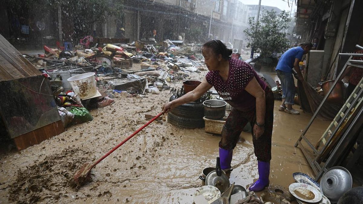 A woman sweeps mud during a rainstorm outside a row of houses which were flooded up to the second floor when a reservoir collapsed near Gantang, in Chinaís southwest Guangxi region, on July 9, 2026. (Photo by GREG BAKER / AFP)