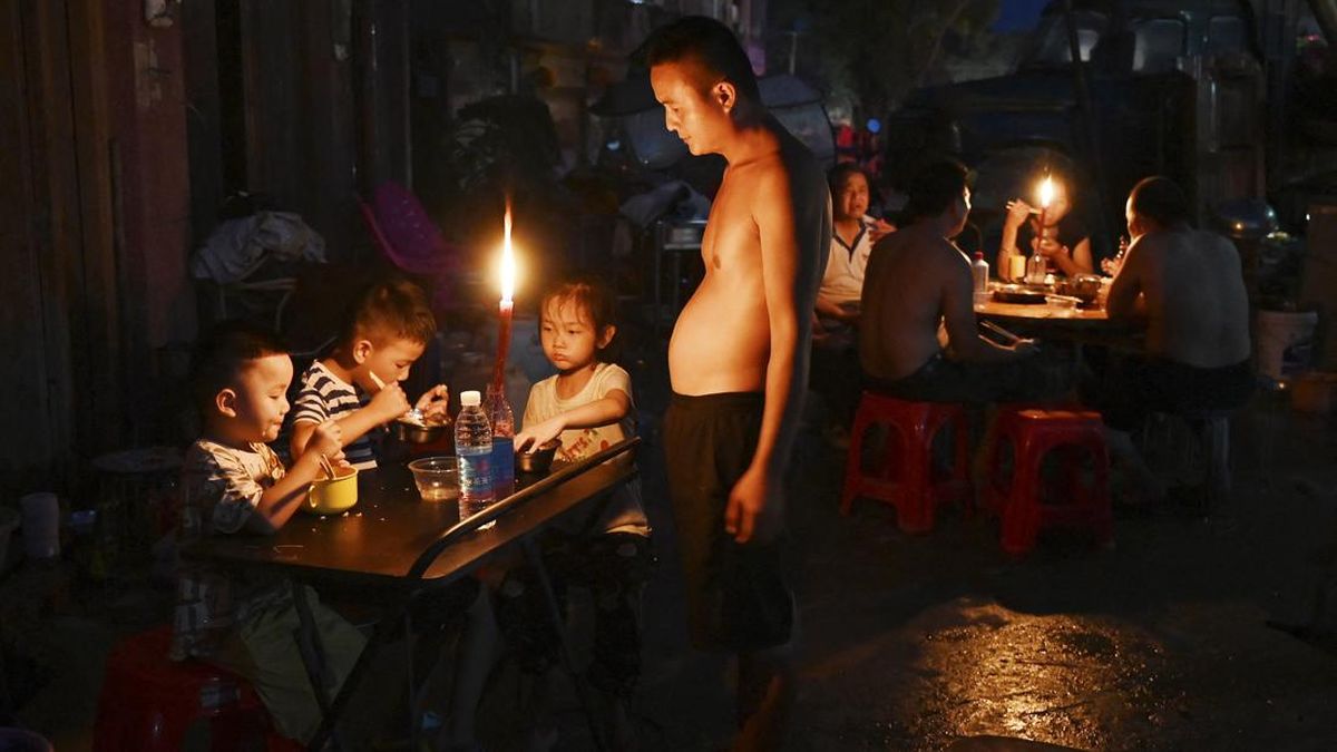 A father looks on as children have dinner by candlelight outside a house in Gantang after electricity was knocked out by floodwaters from a collapsed reservoir in Chinaís southwest Guangxi region on July 9, 2026. The death toll from devastating floo