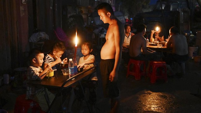 A father looks on as children have dinner by candlelight outside a house in Gantang after electricity was knocked out by floodwaters from a collapsed reservoir in Chinaís southwest Guangxi region on July 9, 2026. The death toll from devastating floo