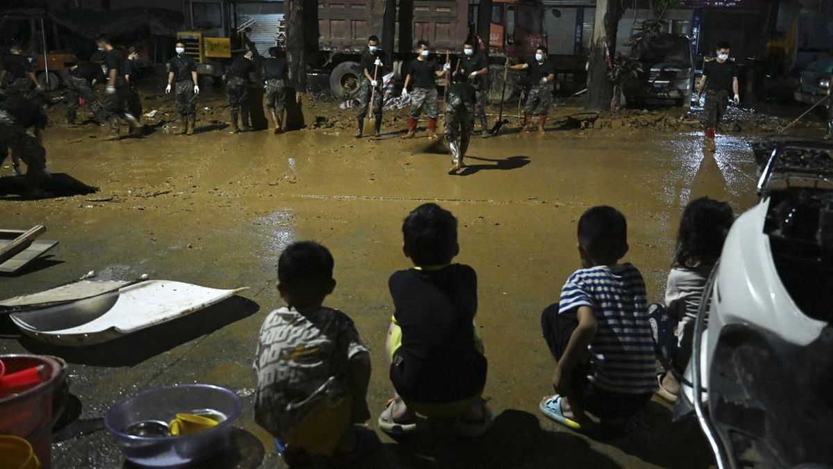 Children look on as security personnel clean mud from a road that was flooded when a reservoir collapsed in Gantang in Chinaís southwest Guangxi region on July 9, 2026. The death toll from devastating floods in southern China's Guangxi region rose t