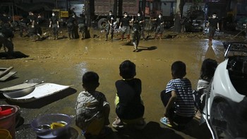 Children look on as security personnel clean mud from a road that was flooded when a reservoir collapsed in Gantang in Chinaís southwest Guangxi region on July 9, 2026. The death toll from devastating floods in southern China's Guangxi region rose t