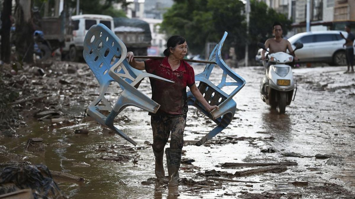 A woman carries chairs along a road during a cleanup operation in Gantang after it was flooded when a nearby reservoir collapsed in Chinaís southwest Guangxi region on July 9, 2026. The death toll from devastating floods in southern China's Guangxi