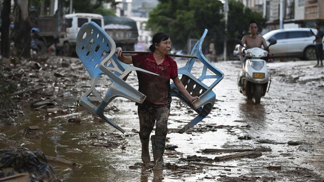 A woman carries chairs along a road during a cleanup operation in Gantang after it was flooded when a nearby reservoir collapsed in Chinaís southwest Guangxi region on July 9, 2026. The death toll from devastating floods in southern China's Guangxi
