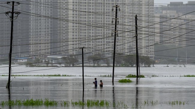 Men wade through a flooded area due to heavy rains in Vasai on July 8, 2026. (Photo by Punit PARANJPE / AFP)