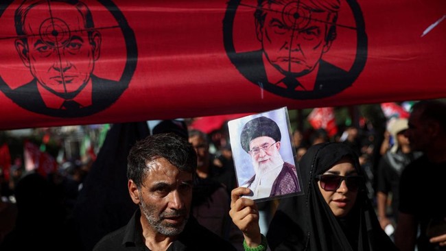 A woman holds a picture of Iran's late Supreme Leader Ayatollah Ali Khamenei as she stands underneath a banner against U.S. President Donald Trump and Israeli Prime Minister Benjamin Netanyahu as mourners gather on the day of the burial of Iran's lat
