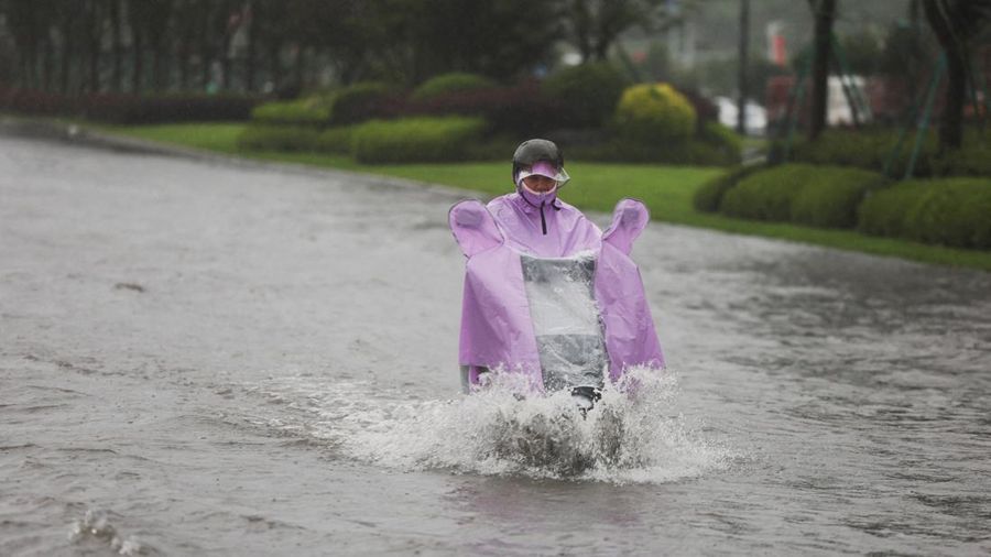 A person rides an electric scooter through a flooded road after heavy rain brought by Typhoon Bavi in Wenzhou, Zhejiang province, China July 12, 2026.
