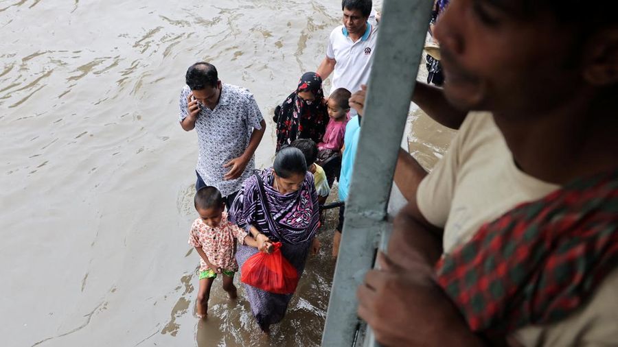 Orang-orang melangkah di sepanjang jalan nan tergenang banjir setelah hujan deras di Dhaka, Bangladesh, 12 Juli 2026.