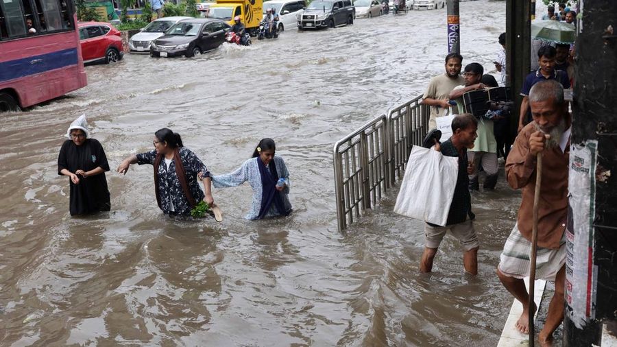 Orang-orang dan kendaraan bergerak melintasi jalan nan tergenang banjir setelah hujan deras di Dhaka, Bangladesh, 12 Juli 2026.