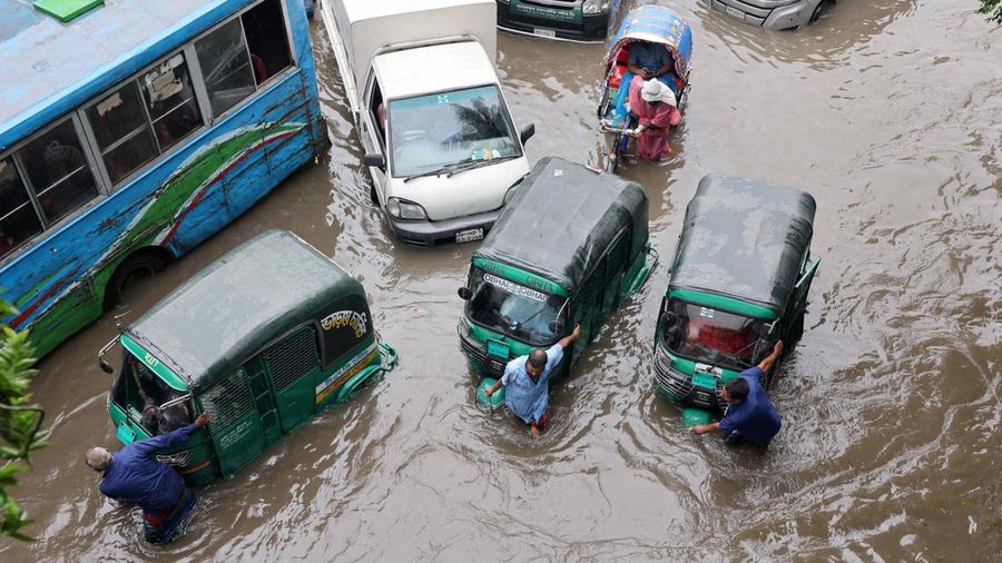 Para pengemudi mendorong becak motor mereka melewati jalan nan tergenang banjir setelah mesin kendaraan mereka mogok akibat hujan deras di Dhaka, Bangladesh, 12 Juli 2026.