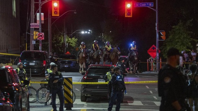 Police officers and other law enforcement personnel block off access to the intersection of St. Clair West and Arlington Avenue, near the site of a shooting that occurred at the Salsa on St. Clair Festival in Toronto on the evening of July 11, 2026.