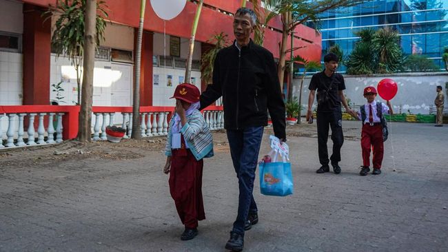 Dua orang tua menggandeng anaknya menuju ruang kelas pada hari pertama tahun ajaran baru di SD Negeri Sudirman, Makassar, Sulawesi Selatan, Senin (13/7/2026). Pemerintah menggelar Gerakan Ayah Mengantar Anak di Hari Pertama Sekolah (GAMAS) untuk mend