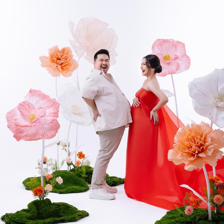 <p>Dalam latar foto dengan gambar bunga ini, Nex juga tetap memberikan citranya yang kocak sebagai food vlogger dengan menyandingkan perutnya dengan baby bump sang istri. Semoga kehamilan anak ketiga mereka berjalan lancar dan sehat hingga persalinan ya Bunda. Foto: Instagram @nexcarlos</p>