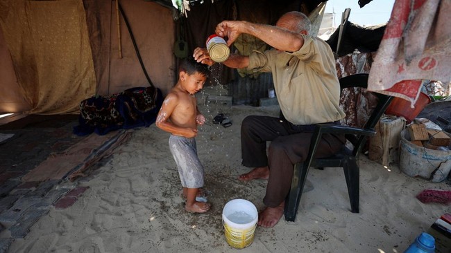 A displaced Palestinian man bathes his grandchild at a tent sheltering displaced people, in Gaza City, July 15, 2026. REUTERS/Dawoud Abu Alkas