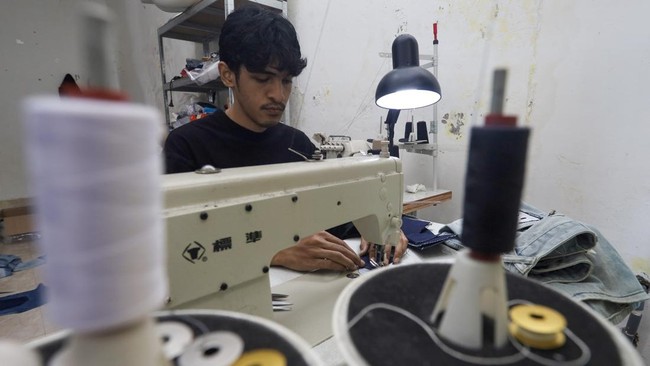 Perajin Bunay Ilhamullah (23) menjahit limbah kain jeans menjadi produk fesyen di rumah produksi Bumoe, Banda Aceh, Aceh.