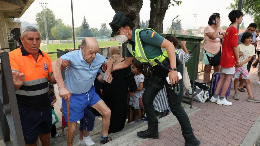 Seorang polisi wanita membantu seorang penduduk lanjut usia nan dievakuasi saat orang-orang berlindung sementara dari kebakaran rimba di wilayah Burgohondo dan San Martin de Valdeiglesias, di arena olahraga kota di Cebreros, Avila, Spanyol, 24 Juli 2026.
