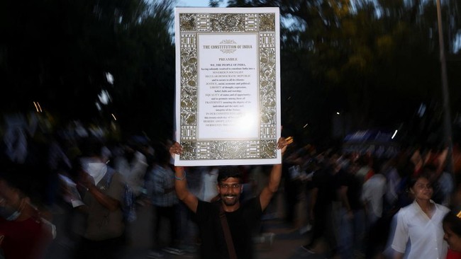 A man holds the Preamble to the Constitution of India as supporters of the Cockroach Janta Party (CJP) celebrate the resignation of Education Minister Dharmendra Pradhan over the National Eligibility cum Entrance Test (NEET) examination paper leaks,