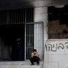 A Palestinian boy sits near a damaged a mosque, which Palestinians say was damaged by Israeli settlers, in Qusra near Nablus, in the Israeli-occupied West Bank, July 26, 2026. Graffiti on the wall reads "Revenge Benayahu", in reference to the 32-year