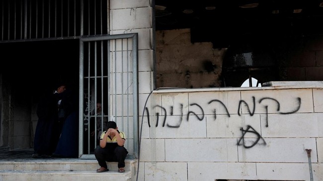 A Palestinian boy sits near a damaged a mosque, which Palestinians say was damaged by Israeli settlers, in Qusra near Nablus, in the Israeli-occupied West Bank, July 26, 2026. Graffiti on the wall reads