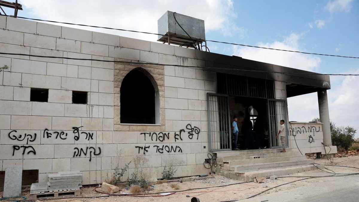 Palestinian boys stand at a damaged a mosque, which Palestinians say was damaged by Israeli settlers, in Qusra near Nablus, in the Israeli-occupied West Bank, July 26, 2026. Graffiti on the wall includes