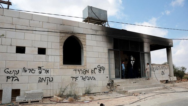 Palestinian boys stand at a damaged a mosque, which Palestinians say was damaged by Israeli settlers, in Qusra near Nablus, in the Israeli-occupied West Bank, July 26, 2026. Graffiti on the wall includes