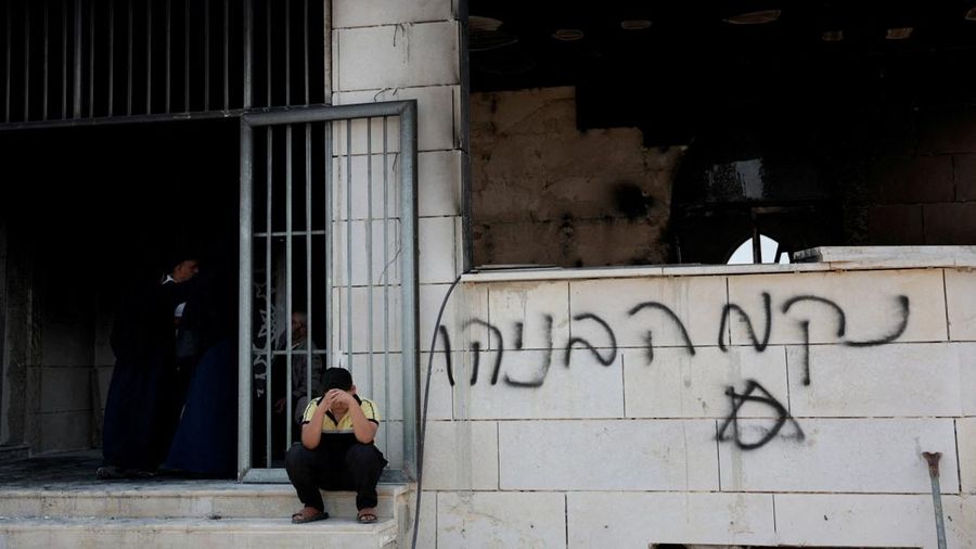 Seorang anak laki-laki Palestina duduk di dekat masjid nan rusak, nan menurut penduduk Palestina dirusak oleh pemukim Israel, di Qusra dekat Nablus, di Tepi Barat nan diduduki Israel, 26 Juli 2026. Grafiti di tembok bertuliskan