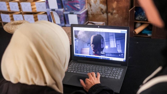 Seorang staf dari Asosiasi Budaya dan Seni Mayasem memeriksa gambar-gambar di laptop, sementara yang lain memperbaiki dan merestorasi secara ilmiah sejumlah artefak yang dikumpulkan selama perang di Gaza, di fasilitas penyimpanan warisan budaya