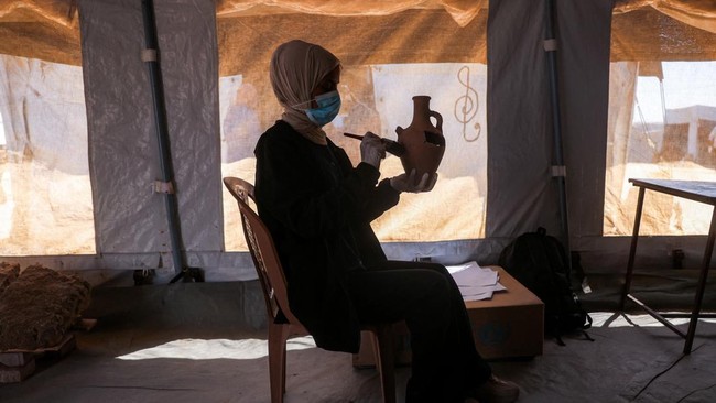 Seorang staf dari Asosiasi Budaya dan Seni Mayasem sedang membersihkan sebuah benda tembikar, sementara yang lain memperbaiki dan merestorasi secara ilmiah sejumlah artefak yang dikumpulkan selama perang di Gaza.