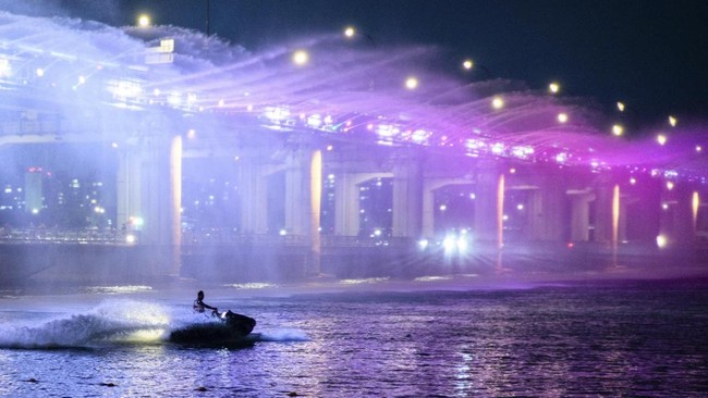 People watch as a jet skier rides near the Moonlight Rainbow Fountain on Banpo Bridge, which stretches over the Han River in Seoul on August 8, 2025. (Photo by Anthony WALLACE / AFP)