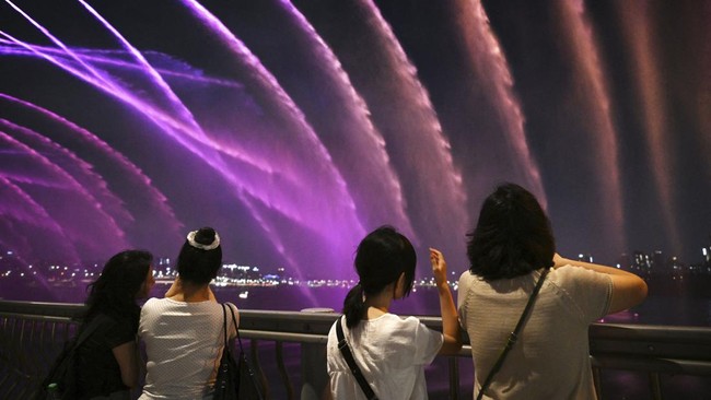People watch the Moonlight Rainbow Fountain on Banpo Bridge, over the Han River in Seoul on July 28, 2026. (Photo by GREG BAKER / AFP)