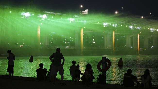 People watch the Moonlight Rainbow Fountain on Banpo Bridge, over the Han River in Seoul on July 28, 2026. (Photo by GREG BAKER / AFP)