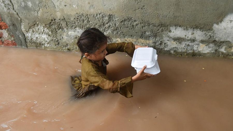Seorang gadis membawa bungkusan makanan sembari menerobos genangan air banjir setelah hujan monsun di Ferozwala, Pakistan, 28 Juli 2026.