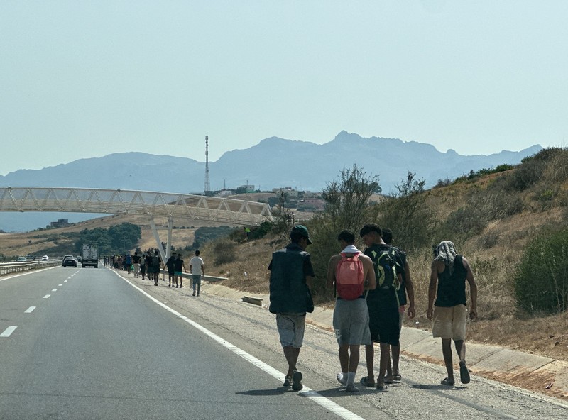 Migrants walk on the Moroccan side of the border, after mass crossings of migrants on foot and by sea from Morocco into Spanish territory, as seen from Cueta, Spain, August 1, 2026. REUTERS/Jon Nazca