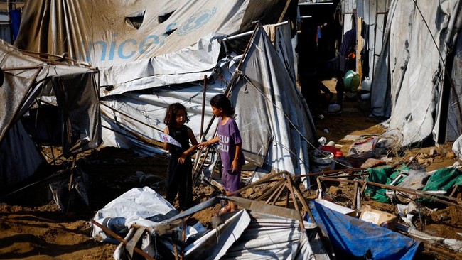 Palestinian children speak to each other near debris, following an overnight Israeli strike on a medicine warehouse, according to medics, in Deir al-Balah, in the central Gaza Strip, August 1, 2026, displaced Palestinians sheltering in the nearby ten