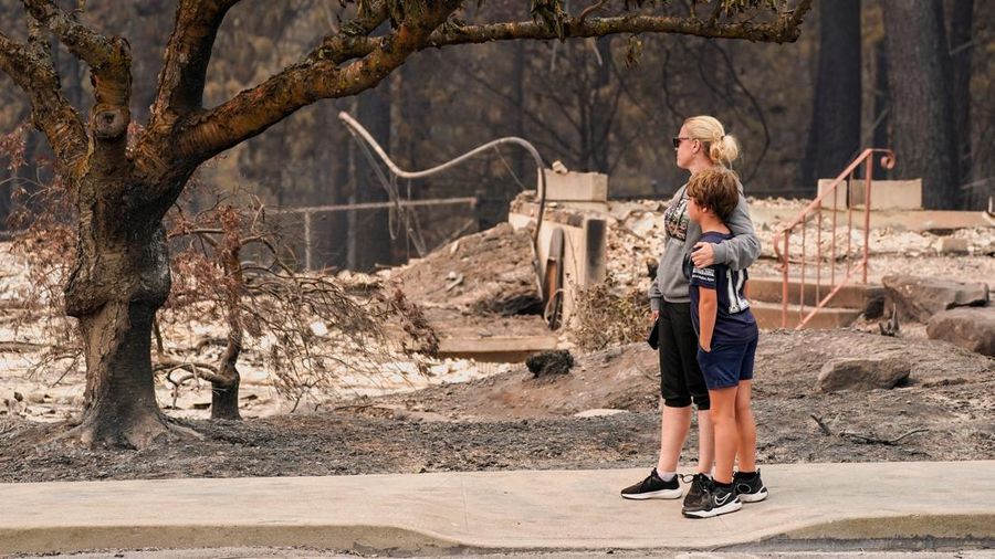 Jana Jensen mengawasi lingkungan tempat rumah masa kecilnya, nan dimiliki oleh orang tuanya, gosong terbakar akibat kebakaran hutan, sembari memeluk putranya, Aaren, 8 tahun, di Spokane, Washington, AS, 2 Agustus 2026.