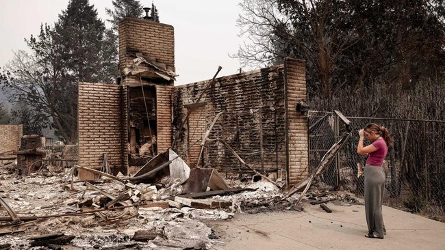 Ash Sollie stands in front of her grandparents' home, where she previously lived, after it was destroyed by a wildfire, in Spokane, Washington, U.S., August 2, 2026. REUTERS/David Ryder     TPX IMAGES OF THE DAY
