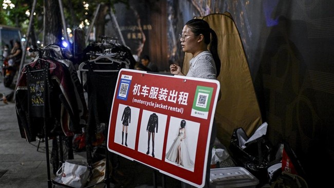 This picture taken on July 21, 2026 shows a motorcycle jacket rental business owner waiting on customers for a riding photo and video service in Chongqing, southwestern China. The roar of engines fills the night air in China's Chongqing city as touri