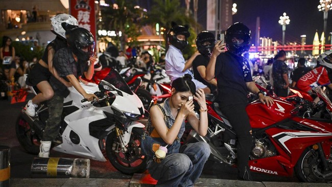 This picture taken on July 20, 2026 shows a woman preparing before going for a motorcycle riding photo and video session in Chongqing, southwestern China. The roar of engines fills the night air in China's Chongqing city as tourists awkwardly clamber