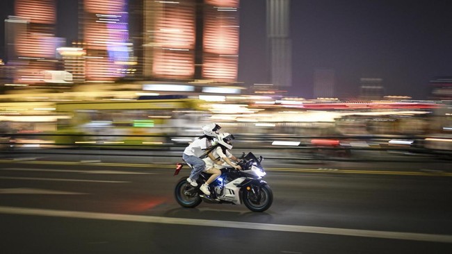 This picture taken on July 20, 2026 shows a woman riding a motorcycle along a street in Chongqing, southwestern China. The roar of engines fills the night air in China's Chongqing city as tourists awkwardly clamber onto gleaming motorbikes and cling