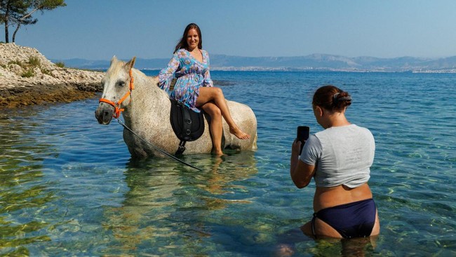 Lana Puscak poses on a horse named 'Perlaz' after swimming with it during a heatwave in Supetar on the island of Brac, Croatia, August 5, 2026. REUTERS/Antonio Bronic