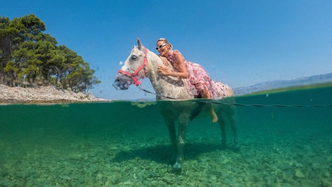A woman poses on a horse named 'Perlaz' after swimming with it during a heatwave in Supetar on the island of Brac, Croatia August 5, 2026. REUTERS/Antonio Bronic REFILE - ADDING DATE