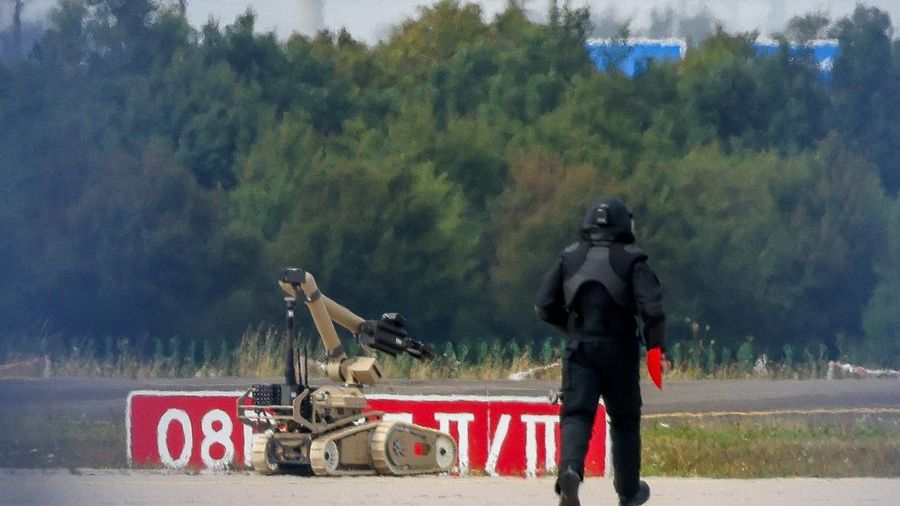 Seorang petugas polisi nan mengenakan busana pelindung melangkah di samping robot penjinak bahan peledak (EOD) di Bandara Leipzig/Halle di Schkeuditz, Jerman, pada 5 Agustus 2026. Langkah ini diambil setelah polisi menyatakan bahwa mahir bahan peledak telah memeriksa sebuah pesawat nirawak (drone) nan ditemukan di dekat landasan pacu, serta menyusul kejadian pesawat kargo DHL nan menabrak objek tak dikenal saat sedang menanjak meninggalkan airport pada malam sebelumnya, nan memicu pendaratan tak teragendakan di Hanover, menurut sumber nan mengetahui peristiwa tersebut.