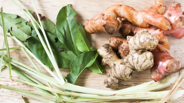 the ingredients for the dish are turmeric&comma; ginger&comma; galangal&comma; bay leaves&comma; and lemongrass&comma; on a wooden table