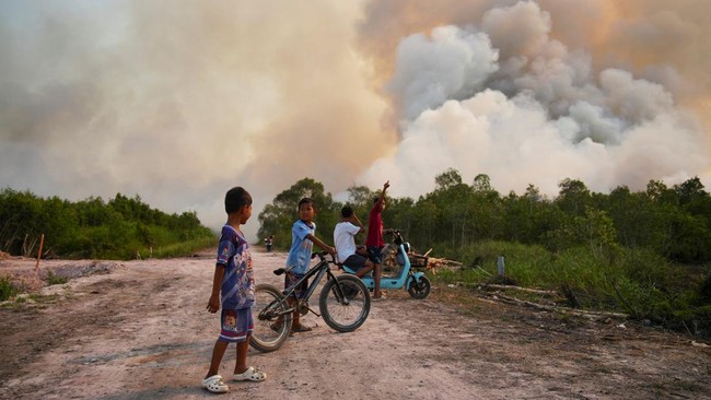 A child sits on an electric scooter as children watch the wildfire in Ogan Ilir regency, South Sumatra province, Indonesia, August 9, 2026. REUTERS/Abriansyah Liberto