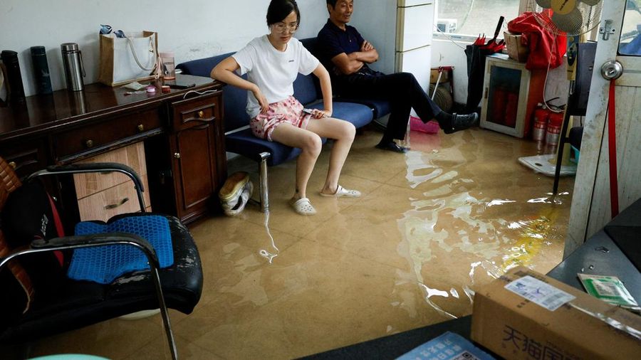 Orang-orang duduk di sofa di dalam ruangan nan terendam banjir setelah Topan Dolphin membawa hujan lebat ke Shanghai, Tiongkok, pada 10 Agustus 2026.