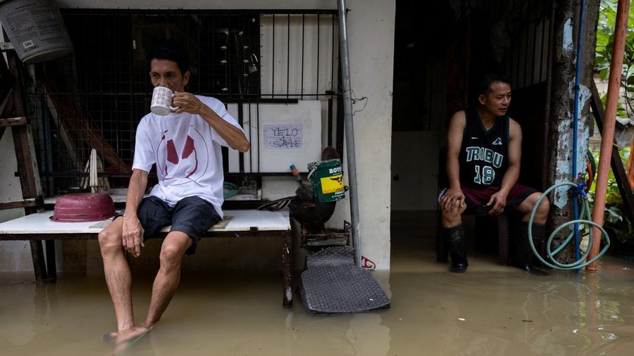 Rolly Gatan minum kopi berbareng tetangganya, Jair Paredes, sembari duduk di rumah Paredes nan terendam banjir akibat hujan monsun barat daya di Bagong Silangan, Quezon City, Filipina, pada 10 Agustus 2026.