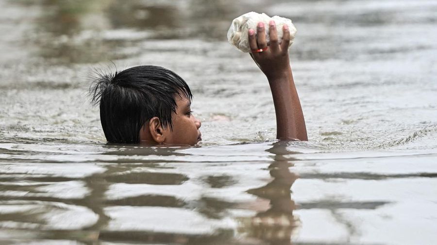 Seorang anak laki-laki memegang lumpia mentah saat melangkah menerjang banjir setelah hujan deras semalam di Barangay Marulas, Kawit, Cavite, Filipina, pada 9 Agustus 2026.