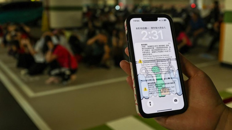 Seseorang memegang ponsel pintar yang menampilkan peringatan darurat nasional—berupa simulasi serangan rudal dan pemberitahuan pengurangan penggunaan data seluler—saat warga berlindung dalam latihan pertahanan udara untuk ketahanan perkotaan yang merupakan bagian dari latihan militer tahunan Han Kuang, di area bawah tanah Stasiun Taichung di Taichung, Taiwan, pada 10 Agustus 2026.