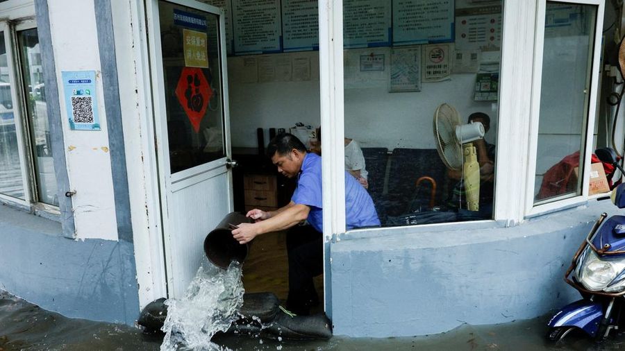 Seseorang menggunakan ember untuk mengeluarkan air dari ruangan nan terendam banjir setelah Topan Dolphin membawa hujan lebat ke Shanghai, Tiongkok, pada 10 Agustus 2026.