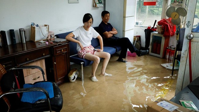 People sit on a sofa in a flooded room after Typhoon Dolphin brought heavy rain to Shanghai, China, August 10, 2026. REUTERS/Go Nakamura