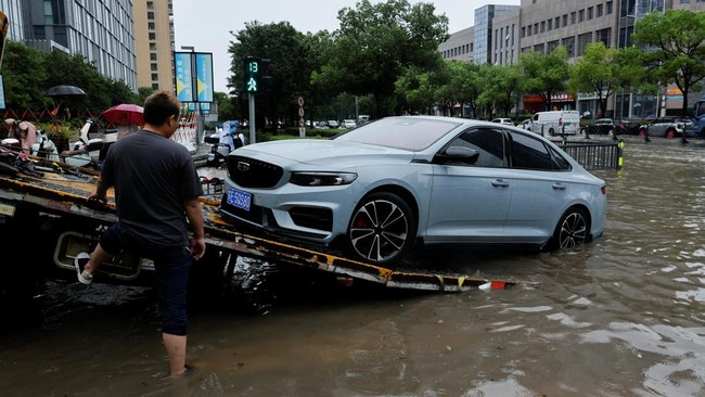 A worker loads a broken-down car onto a car carrier truck on a flooded street after Typhoon Dolphin brought heavy rain to Shanghai, China, August 10, 2026. REUTERS/Go Nakamura